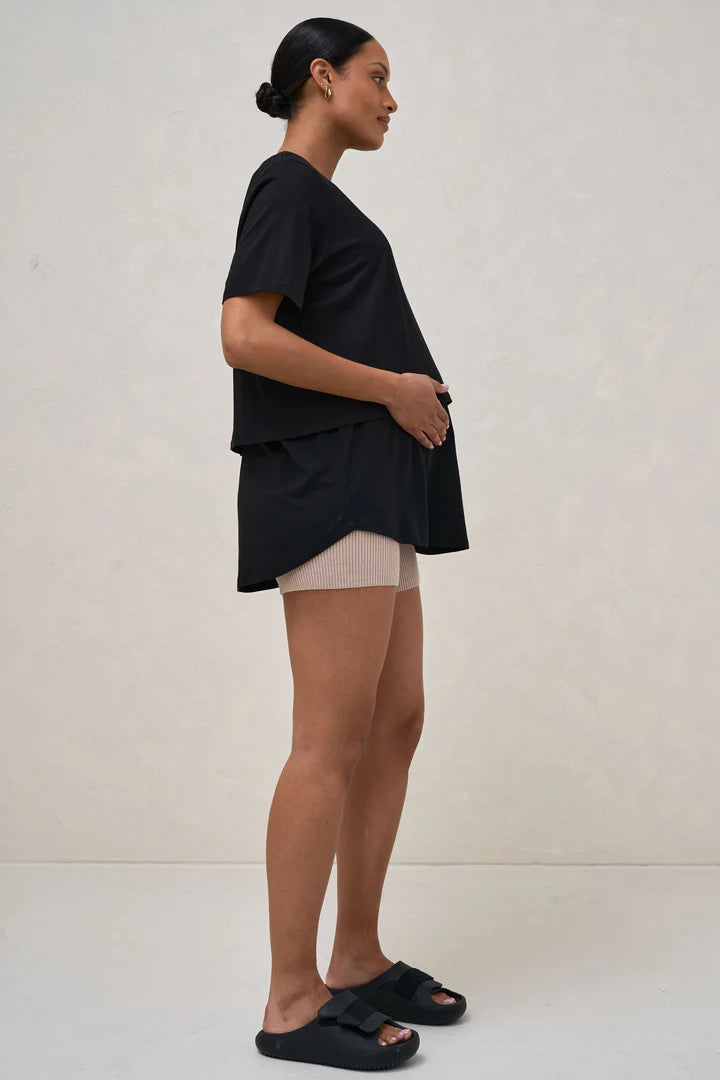 A pregnant woman wearing a black nursing tee with short sleeves and a round neck, paired with beige shorts.