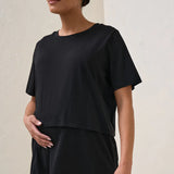 A pregnant woman wearing a black nursing tee with short sleeves and a round neck, paired with beige shorts.
