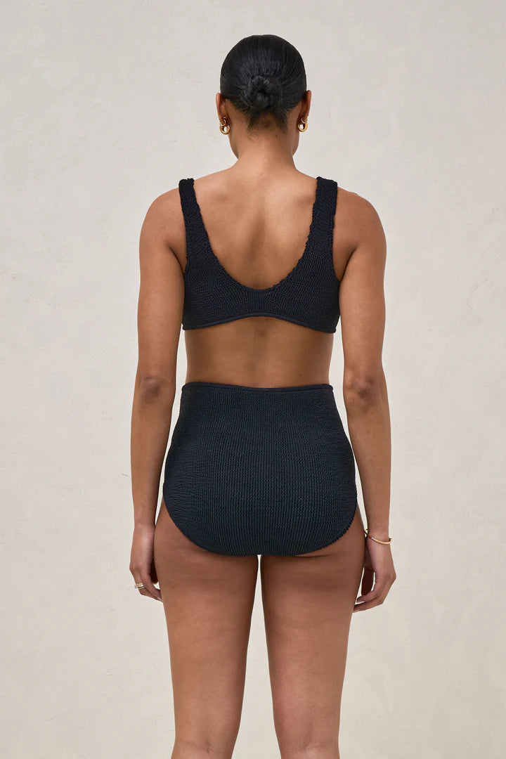 Person wearing a black bikini set on a beige background