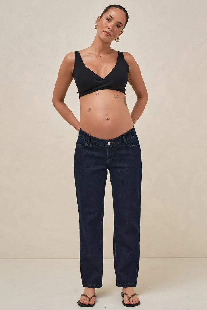 Pregnant woman wearing a black top and dark blue jeans against a beige background