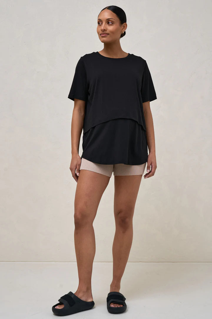 A pregnant woman wearing a black nursing tee with short sleeves and a round neck, paired with beige shorts.