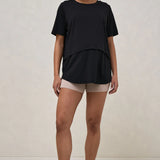 A pregnant woman wearing a black nursing tee with short sleeves and a round neck, paired with beige shorts.