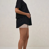 A pregnant woman wearing a black nursing tee with short sleeves and a round neck, paired with beige shorts.