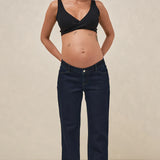 Pregnant woman wearing a black top and dark blue jeans against a beige background