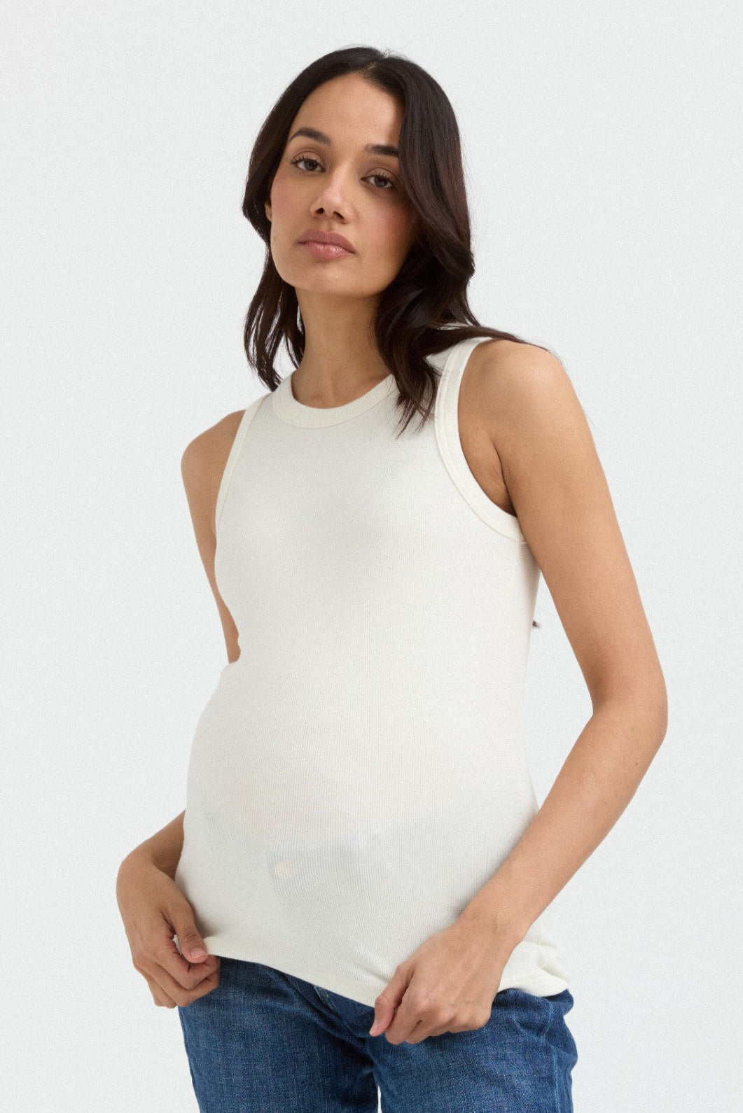 A pregnant woman wearing a white sleeveless ribbed tank top.