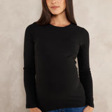 A woman modeling a black long-sleeve crewneck top paired with blue jeans, standing against a textured light gray studio backdrop.