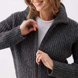 A woman wearing a dark gray ribbed knit zip-up cardigan over a white t-shirt, shown in a close-up shot against a light gray background.