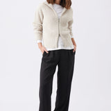 Chunky Zip Knit Maternity Cardigan (Oat) | Ripe Maternity Woman wearing a beige cardigan, white shirt, black pants, and black shoes on a white background