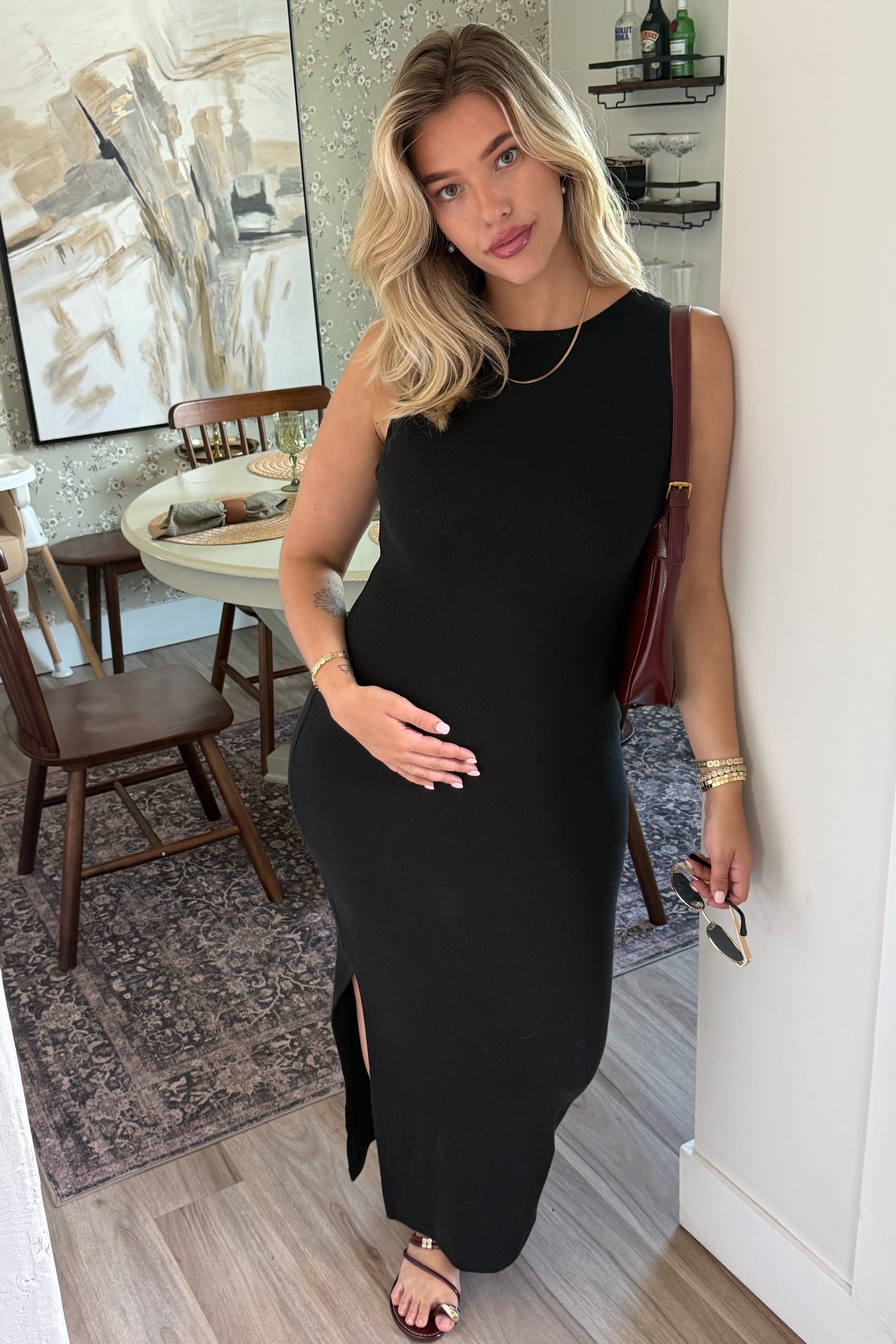 Woman in a black dress standing in a room with a painting on the wall.