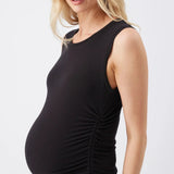 A pregnant woman wearing a black sleeveless maternity tank top with ruching on the side, paired with blue jeans, photographed against a light gray studio background.