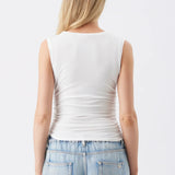 A woman viewed from the back wearing a fitted sleeveless white top and light blue jeans against a plain light gray studio background.