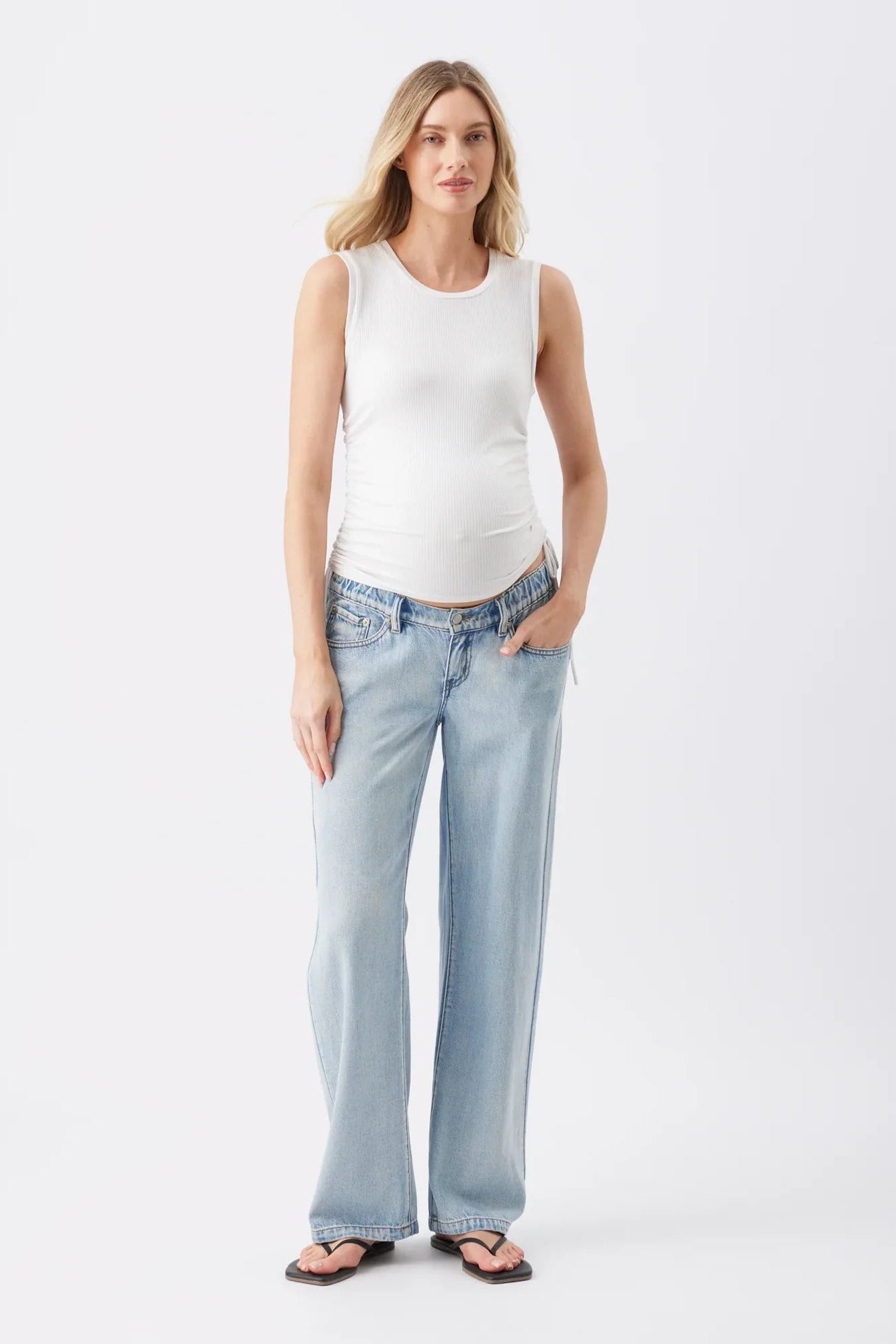 A woman modeling a white sleeveless tank top and light-wash wide-leg jeans against a plain white studio background.