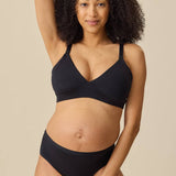 A pregnant model wearing a black maternity bra and matching black underwear, posing against a solid beige background.