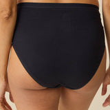 Rear view of a model wearing high-waisted black bikini bottoms against a plain beige background.